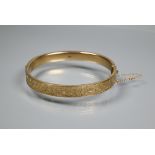 A 9ct yellow gold oval half-hinged bangle with foliate decoration, concealed clasp and safety