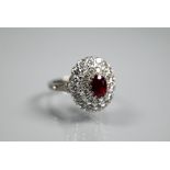 A diamond ruby cluster ring, the oval two row diamond cluster supporting an oval ruby in high claw