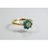 An emerald and diamond daisy ring, the central diamond surrounded by eight small emeralds, yellow