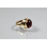 A cabochon garnet set ring in yellow metal setting of plain form, size P, unmarked and untested