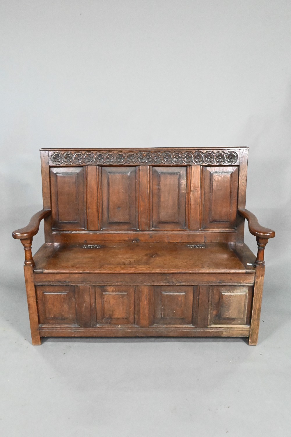 An antique oak box settle, the panelled back with floral carved rosette's over shaped arms and an