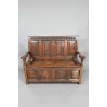 An antique oak box settle, the panelled back with floral carved rosette's over shaped arms and an