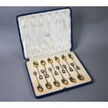 Cased set of twelve Art Deco silver gilt coffee spoons with finials pierced and enamelled with