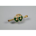 An Edwardian 18ct yellow gold bar brooch featuring two conjoined green and white enamelled hearts,