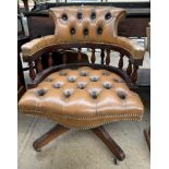 A modern brown leather office swivel chair with button back upholstery on four legs