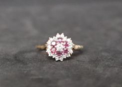 A 9ct gold ruby and diamond cluster ring, set with a central round brilliant cut diamond,