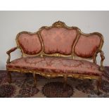 A French carved and gilt decorated three seater settee, carved with scrolling leaves and flowers,