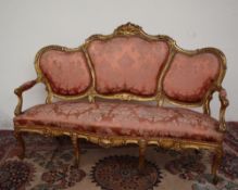 A French carved and gilt decorated three seater settee, carved with scrolling leaves and flowers,