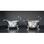 A pair of George V Scottish silver sauce boats with a shaped rim and scrolling handle on three legs,