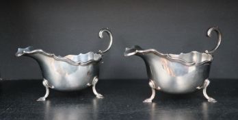 A pair of George V Scottish silver sauce boats with a shaped rim and scrolling handle on three legs,