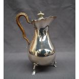 An Edward VII silver hot water jug with a flared edge and baluster body on three legs with trefid