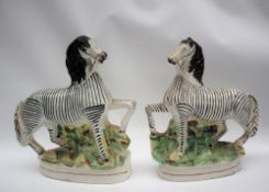 A pair of 19th century Staffordshire zebras, with a raised front leg on an oval base,