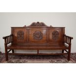 A 20th century oak settle, with a carved scrolling cresting rail above a three panel back,