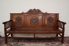 A 20th century oak settle, with a carved scrolling cresting rail above a three panel back,