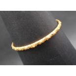 A yellow metal bangle decorated with flower heads, 75mm diameter,
