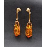 A pair of amber drop earrings in a yellow metal mount and post,