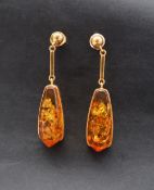 A pair of amber drop earrings in a yellow metal mount and post,