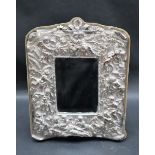 A silver plated easel mirror, profusely decorated with cherubs, flowers and leaves,