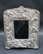 A silver plated easel mirror, profusely decorated with cherubs, flowers and leaves,