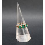 An emerald and diamond line ring set with three oval faceted emeralds and diamond chips to a yellow