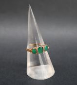 An emerald and diamond line ring set with three oval faceted emeralds and diamond chips to a yellow