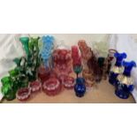A collection of cranberry glass together with blue glass table lustres, green glass ewers,