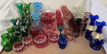 A collection of cranberry glass together with blue glass table lustres, green glass ewers,