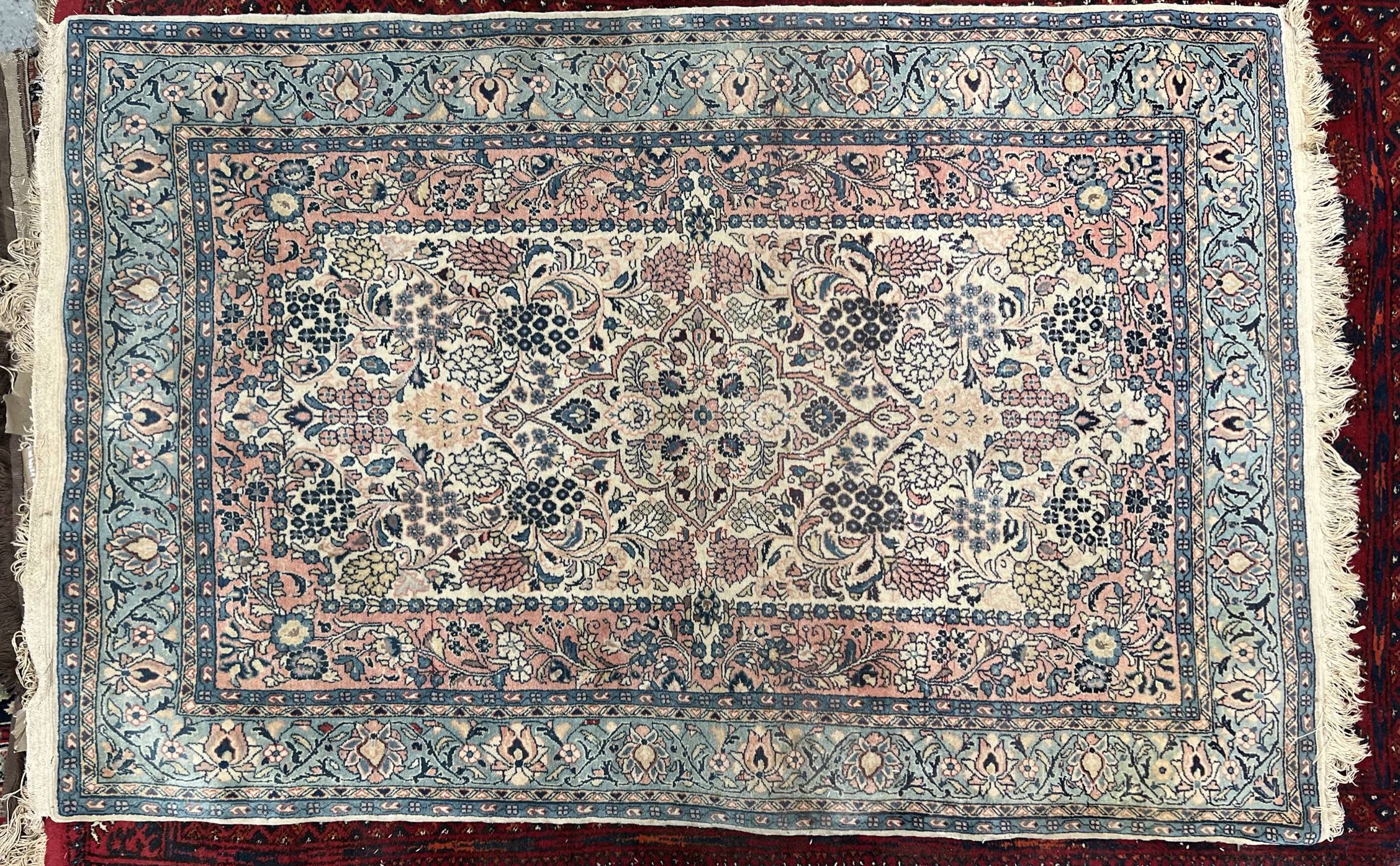 An Iranian rug with a cream ground and scrolling flowers and leaves with pink and blue guard