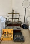 Two balance beam scales together with boxed and loose weights and a magnifying glass on a