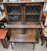 An oak bookcase with leaded glass doors to the top and a cupboard base and an occasional