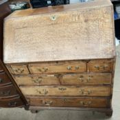 An 18th century oak bureau with a sloping fall enclosing a fitted interior above seven drawers on