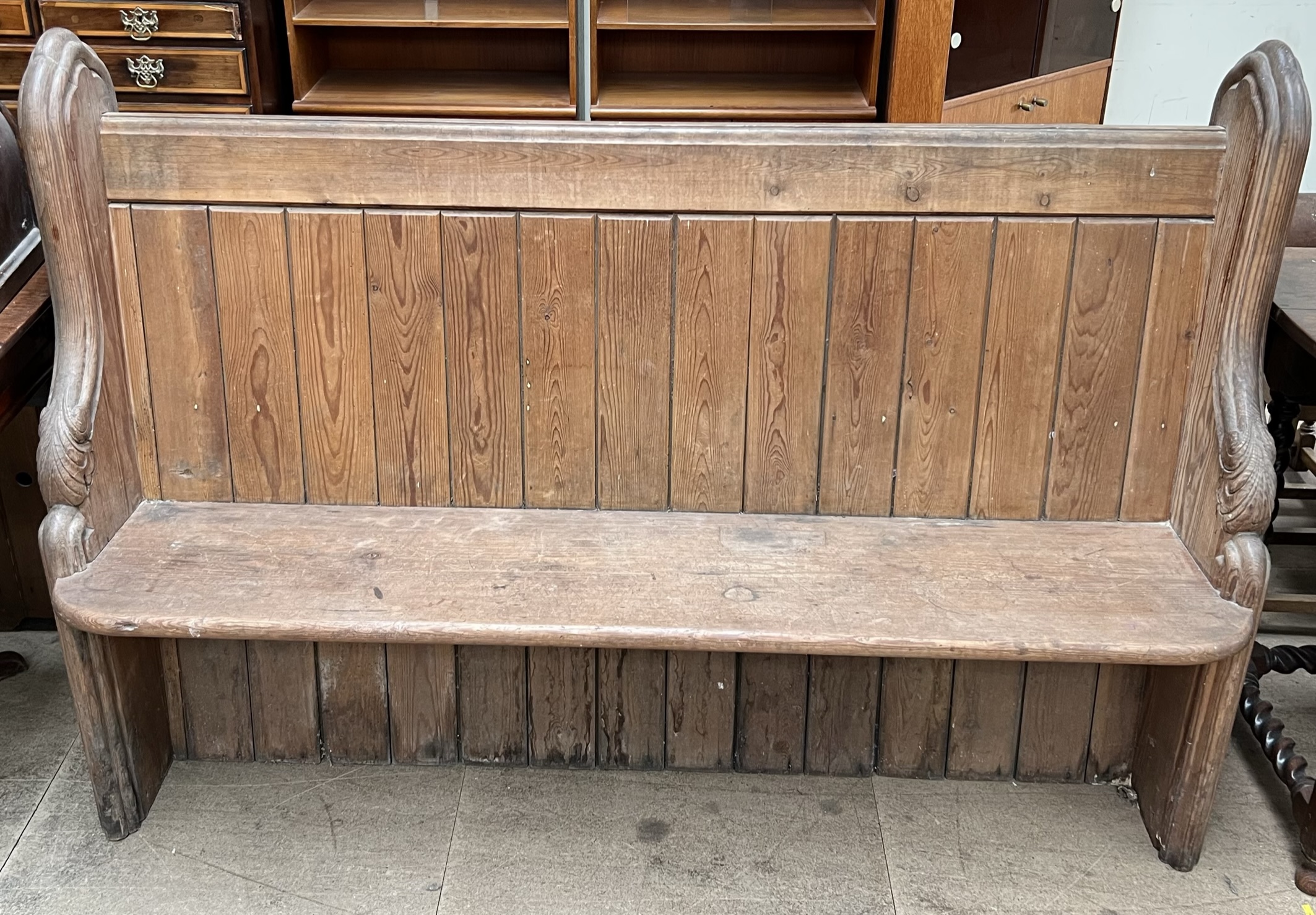 A pine pew bench with carved ends and a panelled back