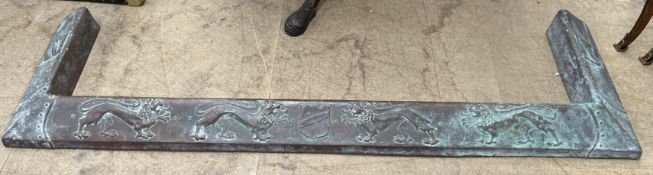A copper fire fender embossed with lions and shields,