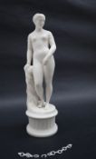 A parian figure of a naked maiden leaning on a pillar, standing on a plinth,