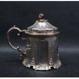 A Victorian silver mustard pot and cover with a floral finial and C scrolling handle to a panelled