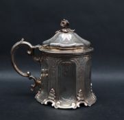 A Victorian silver mustard pot and cover with a floral finial and C scrolling handle to a panelled