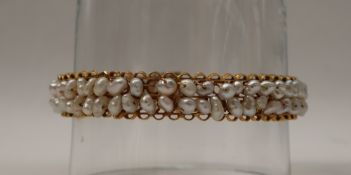 A yellow metal pearl set bangle, with two rows of irregular pearls,
