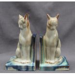 A pair of pottery cat bookends, in greys, blues and greens on a rectangular base,