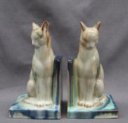 A pair of pottery cat bookends, in greys, blues and greens on a rectangular base,