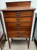 An Edwardian inlaid mahogany music cabinet with a raised back and six drawers with drop fronts on