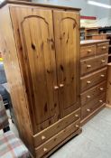 A tall pine chest of drawers together with a pine wardrobe