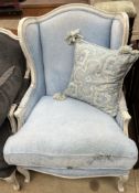 A continental cream painted upholstered wing back chair with pad upholstery and a squab seat on