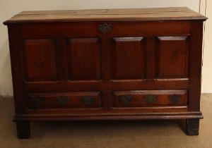 An 18th century oak coffer with a planked rectangular top above a four panel front with faux