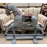 A rocking horse painted grey, with an integral saddle on a fixed base,