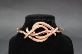 A 9ct yellow gold hinged bangle of knot form with textured bars, approximately 13.