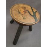 A 20th century milking stool with a circular leather top with a bird holding onto a branch,