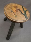 A 20th century milking stool with a circular leather top with a bird holding onto a branch,