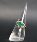 An emerald and diamond cluster ring set with three graduated oval emeralds surrounded by sixteen