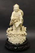 A Chinese Blanc de Chine porcelain figure of a bearded man holding a shoe, standing amongst shells,