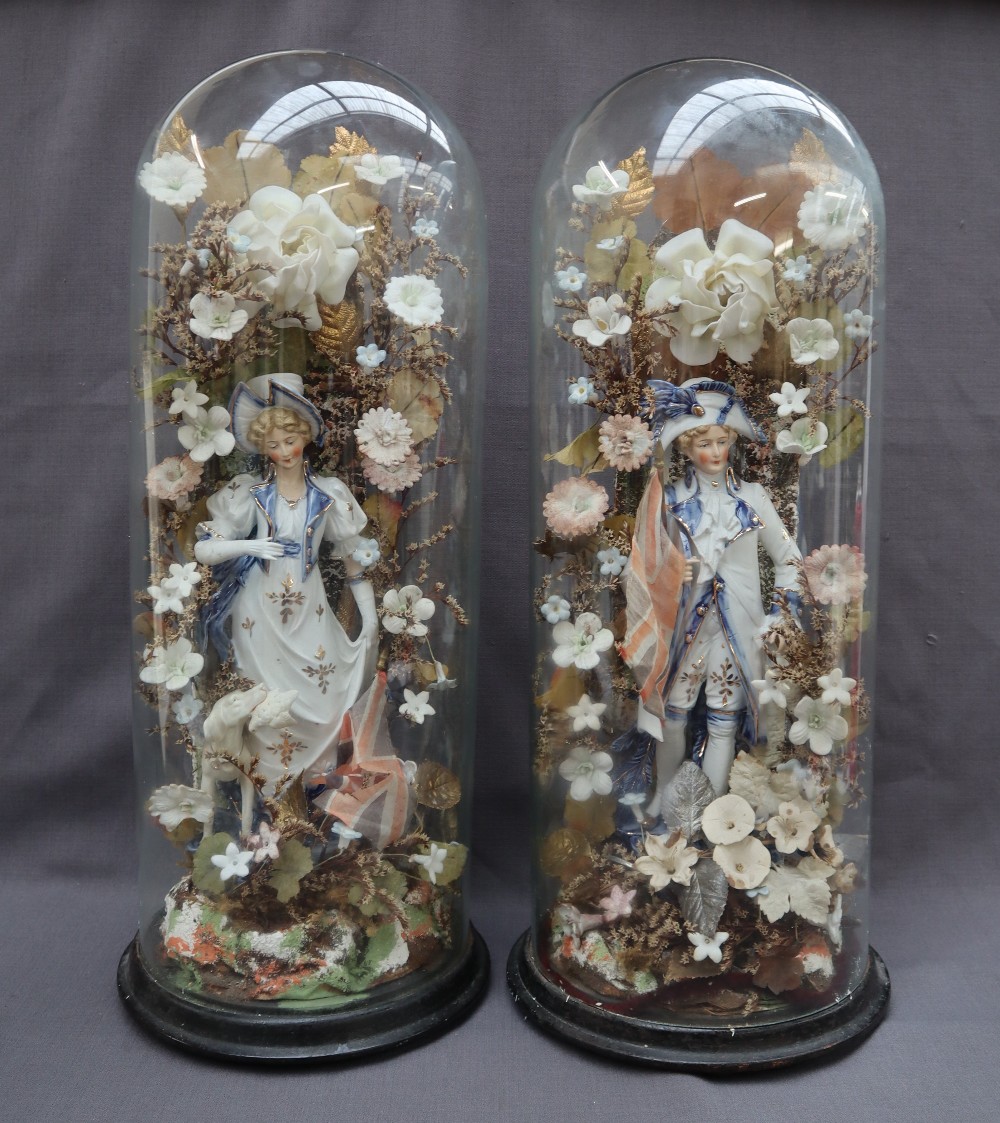 A pair of 19th century continental porcelain figures surrounded by porcelain flowers under glass